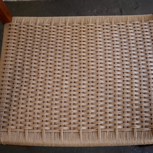 May include: Close-up of a woven chair seat. The seat is made of a light brown material woven in a tight pattern. The chair frame is made of wood. The chair is a neutral color and would fit in any room.