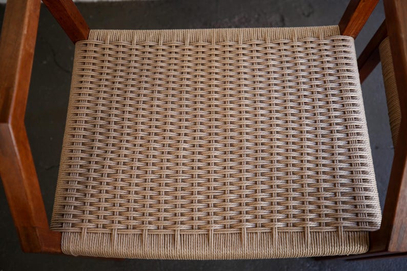 May include: Close-up of a woven chair seat. The seat is made of a light brown material woven in a tight pattern. The chair frame is made of wood. The chair is a neutral color and would fit in any room.