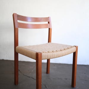 May include: A wooden chair with a woven seat. The chair has a light brown woven seat and a dark brown wooden frame. The back of the chair has two horizontal wooden slats. The chair is on a concrete floor.