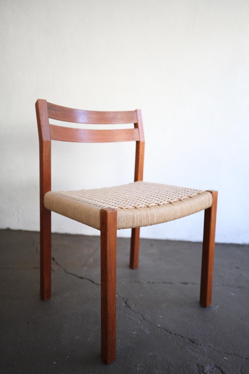 May include: A wooden chair with a woven seat. The chair has a light brown woven seat and a dark brown wooden frame. The back of the chair has two horizontal wooden slats. The chair is on a concrete floor.