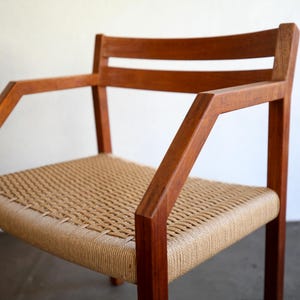 May include: A wooden armchair with a woven seat and back. The chair has a natural wood finish and angled armrests. The seat is made of a light tan woven material. The chair is a mid-century modern style.