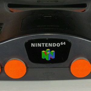 May include: A grey Nintendo 64 console with orange buttons and the Nintendo 64 logo on the front.
