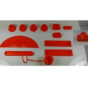 May include: A set of 3D printed orange plastic pieces for a board game. The set includes a variety of shapes, including circles, squares, and rectangles.