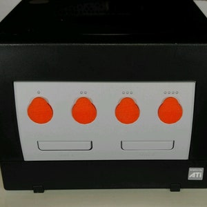 May include: A black gaming console with a white front panel. The front panel has four orange buttons and two slots labelled "GAMEPAK" and "MEMPAK". The console has the text "Graphics by ATI" on the bottom right corner.