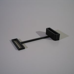 May include: A black plastic belt buckle with a rectangular shape and a small, rectangular opening in the center.