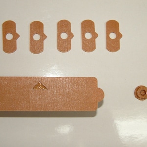 Peut inclure: Un ensemble de pièces en plastique brun pour un kit de modélisme. Les pièces comprennent une longue pièce rectangulaire avec un triangle dessus, six pièces rectangulaires plus petites avec des trous, une petite pièce rectangulaire et une petite pièce ronde.