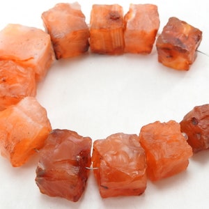 May include: A strand of carnelian beads, each bead is a rough, faceted cube with a deep orange colour. The beads are strung on a silver wire.