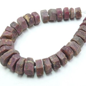 May include: A strand of rough-cut ruby beads. The beads are a deep reddish-purple color with a natural, unpolished texture. The beads are strung together, ready for jewelry making.