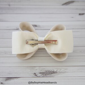 May include: A white satin bow with a silver alligator clip. The bow is tied in a classic style with two loops and a center knot.