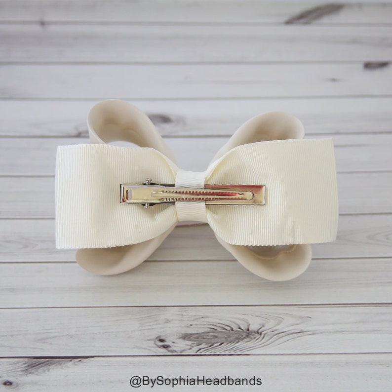 May include: A white satin bow with a silver alligator clip. The bow is tied in a classic style with two loops and a center knot.