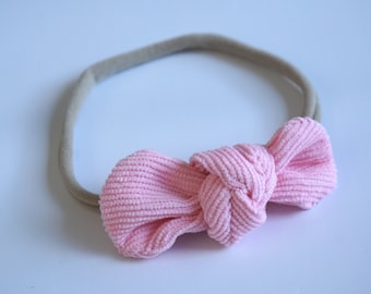 May include: A pink corduroy bow headband with a nude elastic band.