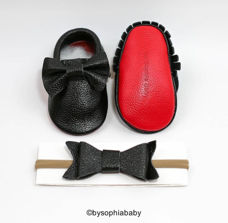 May include: Black leather baby moccasins with a black bow and red soles. A matching black leather headband with a bow is included.