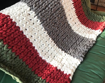 May include: A chunky knit throw blanket with stripes of red, white, gray, and green yarn.