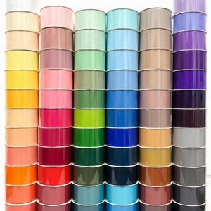 Peut inclure: Une collection de six piles verticales de bobines de ruban disposées selon un spectre de couleurs. Chaque pile contient plusieurs bobines individuelles de ruban de couleur unie, allant du blanc, jaune et orange au rose, vert, bleu et noir.