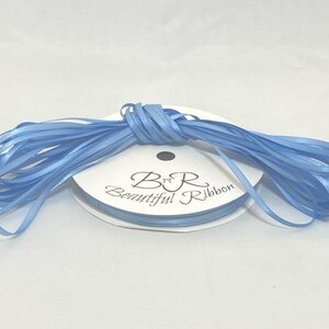 Puede incluir: Un carrete de cinta de raso azul claro. La etiqueta dice "B R Beautiful Ribbon". La cinta est&aacute; cuidadosamente enrollada, adecuada para manualidades o envolver regalos. La cinta mide aproximadamente 0,6 cm de ancho.