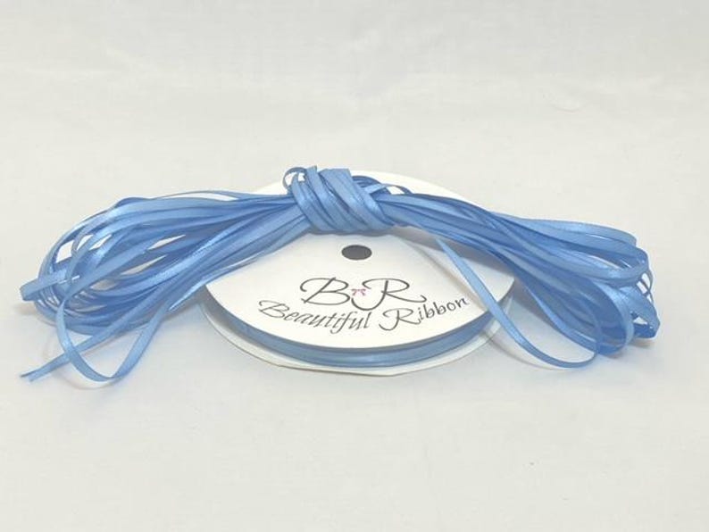Puede incluir: Un carrete de cinta de raso azul claro. La etiqueta dice "B R Beautiful Ribbon". La cinta est&aacute; cuidadosamente enrollada, adecuada para manualidades o envolver regalos. La cinta mide aproximadamente 0,6 cm de ancho.