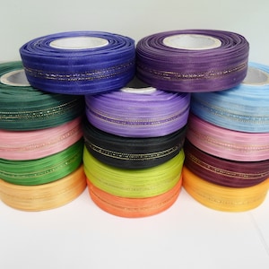 Może przedstawiać: Zestaw 12 szpul wstążki z złotą lamówką. Wstążka jest w różnych kolorach, w tym fioletowym, niebieskim, zielonym, różowym, pomarańczowym i żółtym.