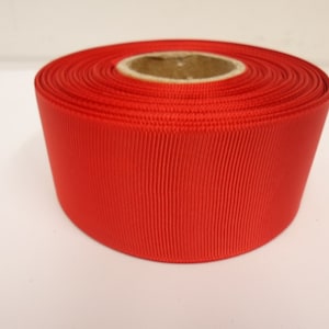 Op de afbeelding: Een rol felrode grosgrain lint. Het lint is gewikkeld om een kartonnen kern.