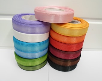 May include: A collection of twelve spools of satin ribbon stacked in two columns. The colors include light pink, lavender, white, bright blue, light green, dark green, yellow, orange, red, magenta, brown, and black, all featuring a smooth finish.