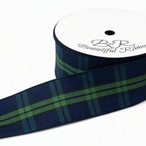 Pode incluir: Um carretel de fita de tecido com um padrão xadrez em azul marinho escuro e verde floresta. A etiqueta circular branca no topo do carretel exibe o texto "B R Beautiful Ribbon" com um pequeno ícone de laço rosa entre as letras B e R.