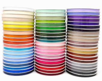 May include: Three vertical stacks of colorful satin ribbon spools arranged in a spectrum of hues including white, yellow, orange, pink, blue, green, purple, brown, gray, and black. Each spool features a smooth, shiny finish and a consistent width.