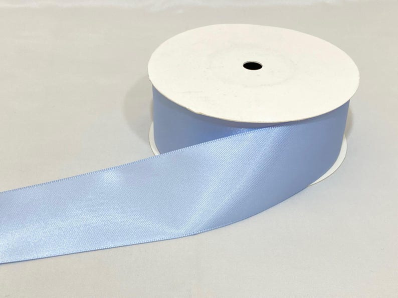 Puede incluir: Un rollo de cinta de raso azul claro. La cinta est&aacute; desenrollada, revelando una textura suave y brillante. El rollo tiene un n&uacute;cleo de cart&oacute;n blanco y cinta azul claro enrollada alrededor. Ideal para manualidades, envolver regalos y decoraciones.