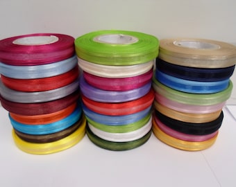 May include: Three vertical stacks of circular ribbon spools in a variety of colors including magenta, light blue, red, gray, burgundy, orange, cyan, brown, yellow, lime green, cream, purple, navy, pink, black, and gold with a smooth texture.