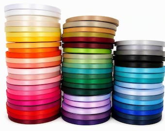 May include: Three vertical stacks of circular ribbon spools in a wide variety of colors including white, yellow, orange, pink, red, green, blue, purple, gray, and black. Each spool features a smooth, satin-like finish with a consistent width.