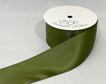May include: A spool of olive green satin ribbon with the text "B&R Beautiful Ribbon" printed on the white label. The ribbon is unwound, showing its smooth texture and color.