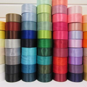 Puede incluir: Una colecci&oacute;n de rollos de cinta de raso apilados en varios colores, incluyendo blanco, amarillo, marr&oacute;n, azul, verde, rosa, rojo y naranja. Los rollos est&aacute;n cuidadosamente dispuestos, mostrando un espectro de tonos para manualidades o decoraci&oacute;n.