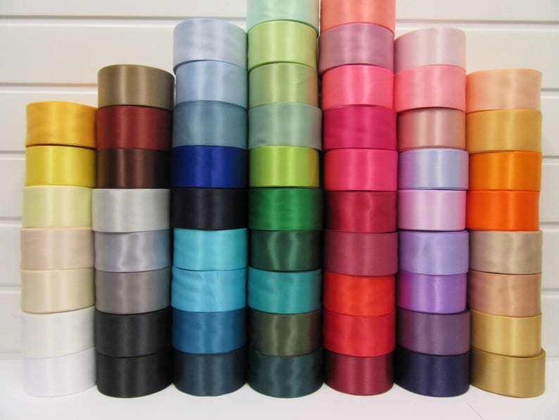 Puede incluir: Una colecci&oacute;n de rollos de cinta de raso apilados en varios colores, incluyendo blanco, amarillo, marr&oacute;n, azul, verde, rosa, rojo y naranja. Los rollos est&aacute;n cuidadosamente dispuestos, mostrando un espectro de tonos para manualidades o decoraci&oacute;n.