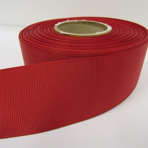 Könnte beinhalten: Eine Rolle rotes Grosgrainband. Das Band ist 2,5 cm breit und hat eine satinierte Oberfläche.