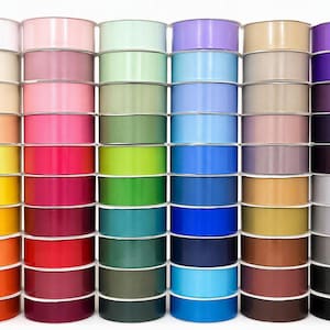 May include: A collection of thirty-six spools of satin ribbon arranged in a grid of six columns and six rows. The spools display a wide spectrum of colours including white, pink, green, blue, purple, yellow, orange, brown, grey, and black.