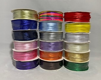 May include: A stack of 15 spools of satin ribbon in various colors, including gold, silver, red, blue, green, pink, and yellow. The spools are arranged in a vertical stack, with the colors alternating.