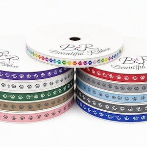 Pode incluir: Dez carretéis de fita gorgorão empilhados em duas colunas, cada um com um padrão repetitivo de pegadas brancas. Os carretéis trazem o texto BR Beautiful Ribbon. As cores incluem roxo, branco, verde, bege, rosa, vermelho, cinza, azul claro, cinza escuro e azul.