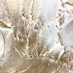 Close up of a shimmering textured surface. The surface is rough, leafy like, painted in pearl white with gold contrast.