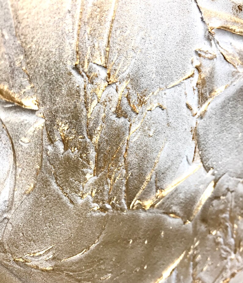 Close up of a shimmering textured surface. The surface is rough, leafy like, painted in pearl white with gold contrast.