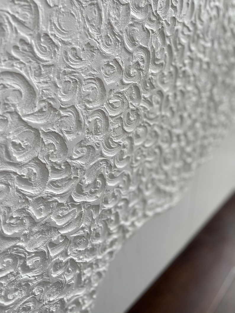 Close-up of a textured white surface with intricate swirls and patterns, reminiscent of bespoke furniture designs. The surface appears sculpted or embossed, creating a three-dimensional effect. At the bottom, theres a smooth transition to a plain white section.