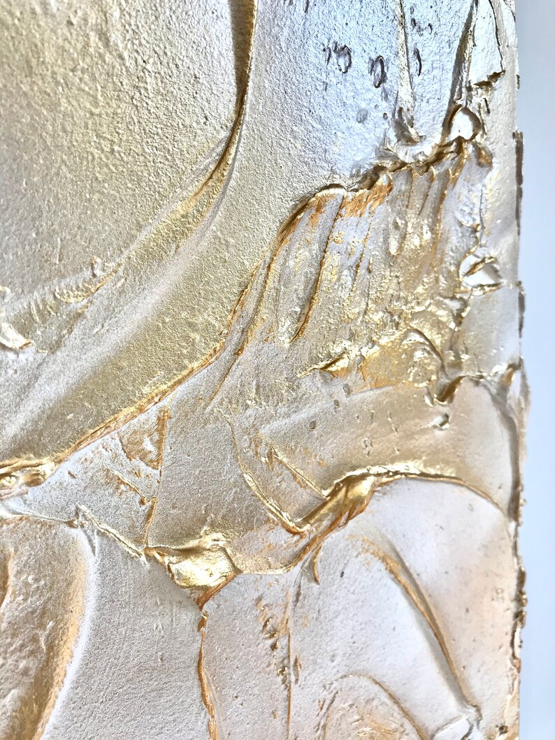 Close up of a shimmering textured surface. The surface is rough, leafy like, painted in pearl white with gold contrast.