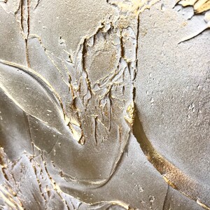 Close up of a shimmering textured surface. The surface is rough, leafy like, painted in pearl white with gold contrast.
