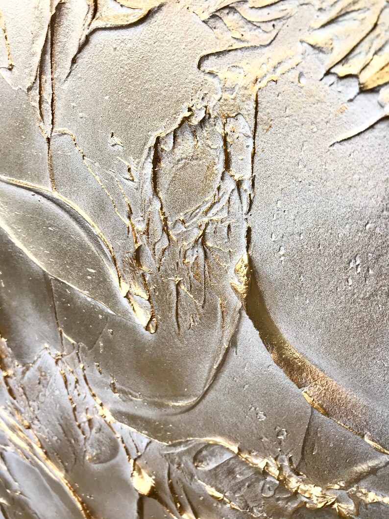 Close up of a shimmering textured surface. The surface is rough, leafy like, painted in pearl white with gold contrast.