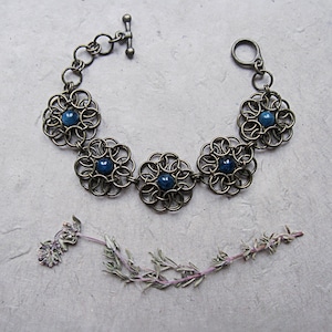 Könnte beinhalten: Ein Armband aus Bronzekette mit vier blauen Edelstein-Blumenakzenten. Das Armband hat einen Toggle-Verschluss.