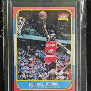 May include: A Fleer Premier basketball trading card featuring Michael Jordan in a red Chicago Bulls uniform with the number 23, performing a slam dunk. The card includes the text Michael Jordan, Bulls, Guard-Forward, and the Fleer Premier logo.