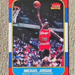 May include: A rectangular Fleer Premier basketball trading card featuring Michael Jordan in a red Chicago Bulls uniform, number 23, performing a slam dunk. The card has a red, white, and blue border with the text Michael Jordan, Bulls, Guard-Forward.