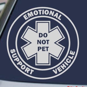 Puede incluir: Calcomanía blanca con el texto "EMOTIONAL SUPPORT VEHICLE" en un diseño circular. El centro presenta un símbolo blanco de la estrella de la vida con las palabras "DO NOT PET". La calcomanía está sobre un fondo azul oscuro.