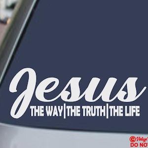 May include: White vinyl decal with the word "Jesus" in a cursive font, with the text "THE WAY | THE TRUTH | THE LIFE" below it. The decal is on a dark blue background, likely a car window.