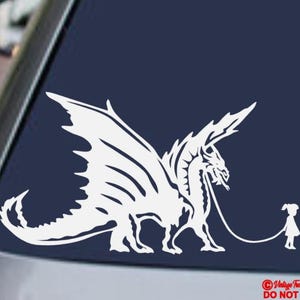 May include: A white vinyl decal featuring a dragon on a leash being held by a small figure. The dragon has large wings and a long tail. The decal is on a dark blue background. Text at the bottom reads "Vintage Treasures Galore DO NOT COPY!"
