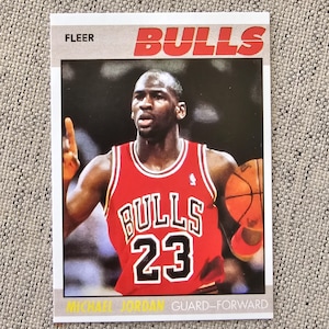 May include: A Fleer trading card featuring Michael Jordan in a red Bulls jersey with the number 23. The card has the word "Bulls" in red block letters at the top and the words "Guard-Forward" at the bottom.