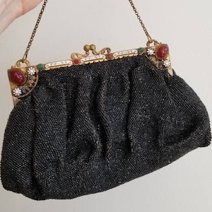 May include: A black beaded evening bag with a gold metal clasp adorned with colourful stones. The bag has a chain strap.