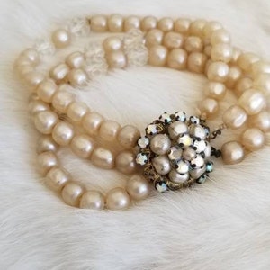 Puede incluir: Un collar de perlas de tres hileras con un gran colgante adornado con pedrería y perlas.